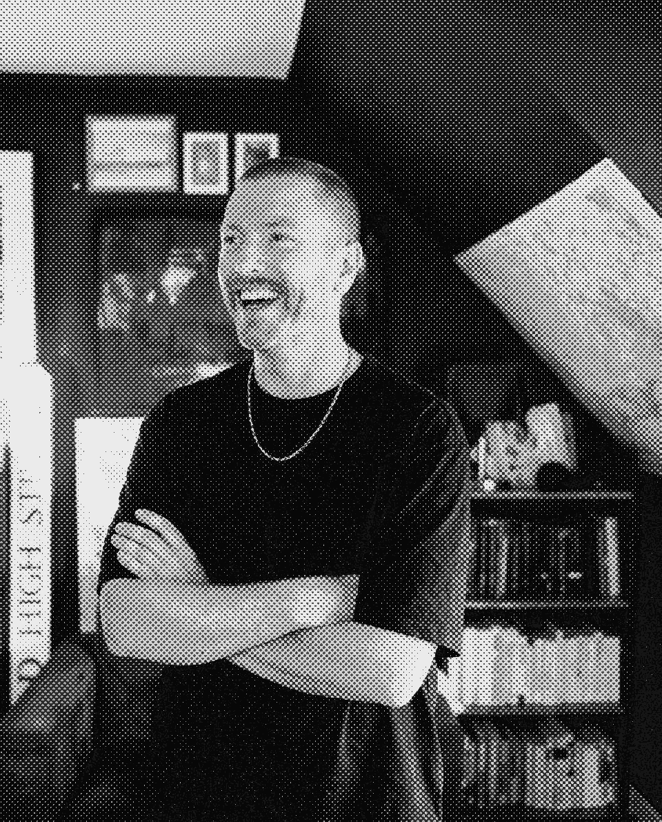 Stu by the studio bookshelf, arms crossed, caught mid-laugh